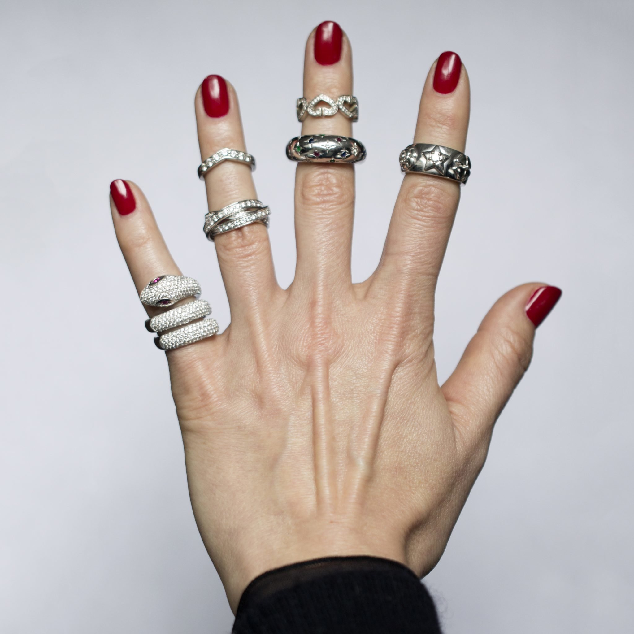 Women's Hand with Red Nail Polish and multiple sterling silver rings and diamond rings on each finger